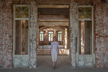 An adult smiling woman stands in the doorway of a hall of an abandoned ancient castle or palace.