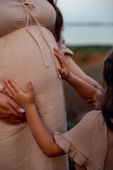 little girl holds hands on her mother's pregnant belly. second third child in family, third...
