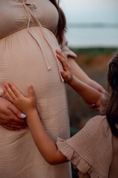 little girl holds hands on her mother's pregnant belly. second third child in family, third trimester of pregnancy. Large family, love and jealousy for parents. Concept of prenatal period, health
