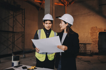 Construction manager and engineer dressed in orange work vests and hard helmets explore...