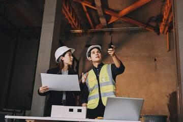 Construction manager and engineer dressed in orange work vests and hard helmets explore construction documentation on the building site near the steel frames