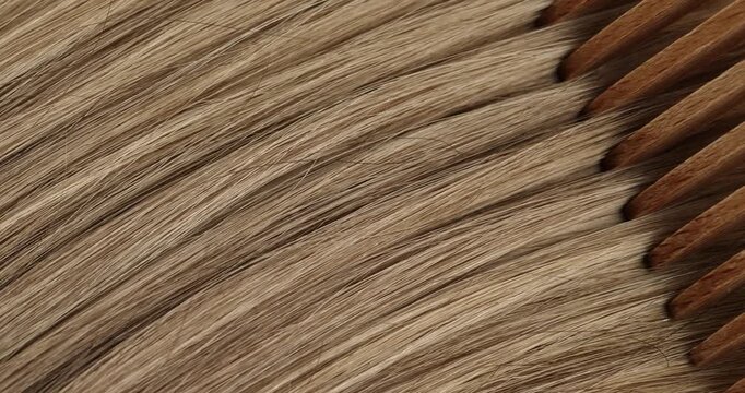 Hair is being combed with a wooden comb in a close-up video.