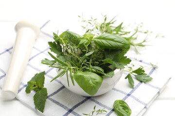 Mortar with different fresh herbs and pestle on white wooden table, closeup