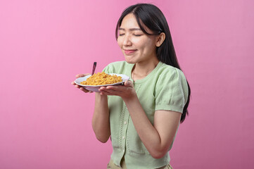 Asian woman in green top looking down at a plate of cooked instant noodles with a spoon, smiling...
