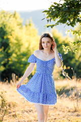 Young woman in blue floral dress enjoys sunny day outdoors in natural setting