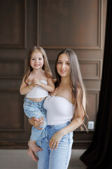 Mother smiles while holding her daughter in stylish casual outfits at home