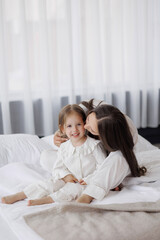 Mother and daughter share a joyful moment in a bright, cozy bedroom setting during the morning
