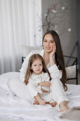 Mother and daughter relaxing together in cozy white bed linens during morning light