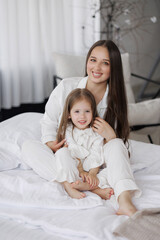 Mother and daughter enjoying a cozy moment at home in white pajamas