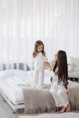 Mother playing with her daughter in bright, cozy bedroom on a calm morning