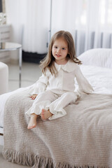 Young girl in white pajamas sitting comfortably on a bed in a cozy room