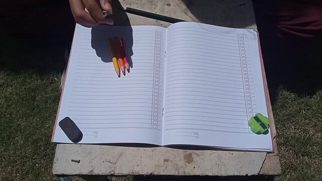 Hand organizing scattered colored pencils into a row next to a book.