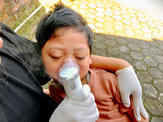 Father giving nebulizer therapy to his sick son outdoors