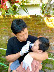 Father giving nebulizer therapy to his sick son outdoors
