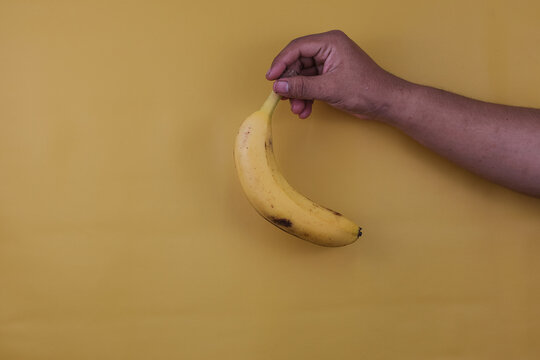 Hand a man hold banana on a yellow background with copy space. Nutrition concept.
