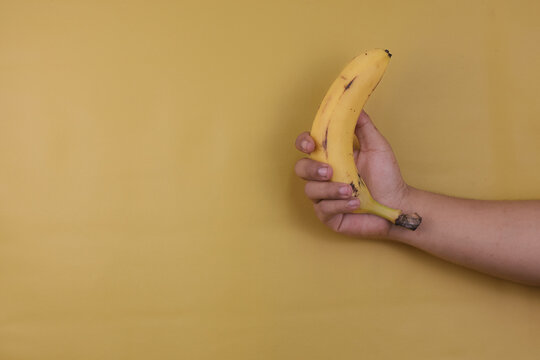 Hand a man hold banana on a yellow background with copy space. Nutrition concept. - Powered by Adobe