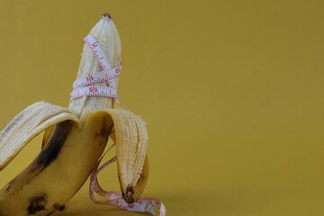 Close up peeled banana with white measurement tape. Men penis sizes concept isolated on yellow...