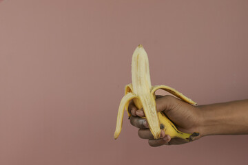 Hand a man hold peeled banana on a brown background with copy space. Nutrition concept.