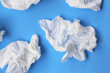 Used crumpled tissues scattered on a blue surface.