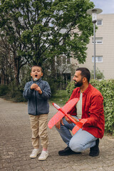 Father and son launch a red toy airplane and blow dandelions while walking in the park. Parenting...