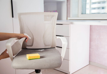 Women's hands wash dirty spots from gray upholstery of computer chair. Concept of dry cleaning of...