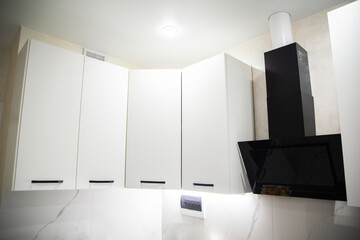Black modern kitchen range hood against white kitchen cabinets, close-up