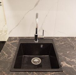 Black modern sink with water tap built into granite worktop in kitchen, industry