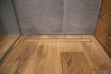 Water drain in brown wood effect tile on floor in shower without trap. Copy space for text