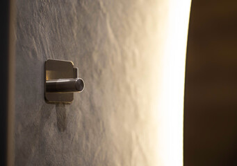 Hook hanger in the bathroom on the wall against the background of a mirror and yellow diode strip,...
