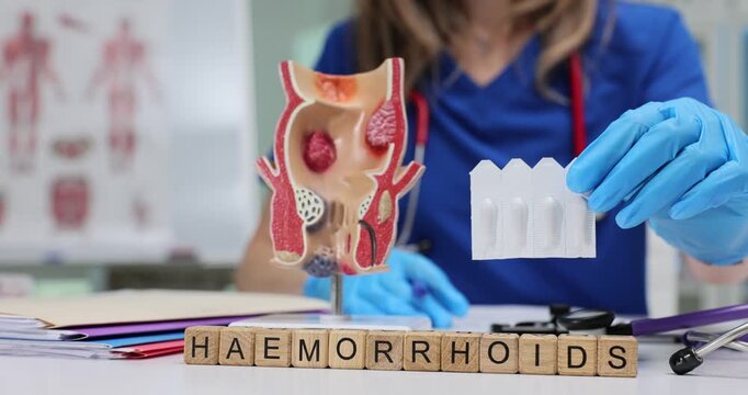 Wooden blocks with Hemorrhoids on desk near model of rectum and woman holding strip of suppositories. Focus on diagnosis and treatment of condition