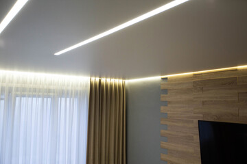 Beautiful modern stylish ceiling with light lines against the background of a window with curtains...