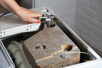 A washing machine repairman tightens the counterweight in the washing machine due to noise and...
