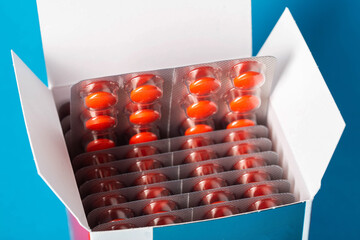 Blisters with red pills in a package on a blue background. Concept of antibiotics in the treatment...