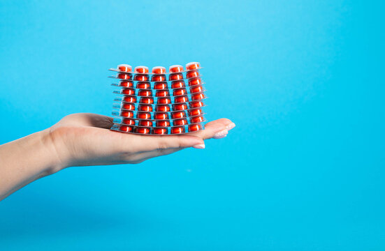 Stack of red pills on palm in hand on blue background. Concept of fluoroquinolone antibiotic pills in treatment of diseases. Copy space for text, closeup