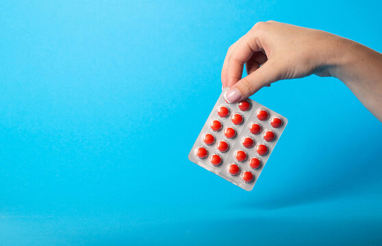 Female hand holding blisters with red pills on blue background. Concept of sedatives in pharmaceuticals. Sedatives and calming drugs. Copy space for text
