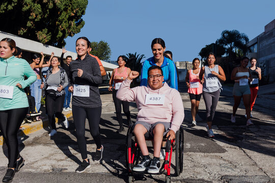 Latin young man on wheelchair competing in a marathon race in the streets in Mexico Latin America, diverse group of hispanic runners, social inclusion concept