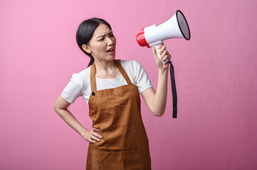Asian woman in brown apron holding a white and red megaphone, appearing to speak confidently,...