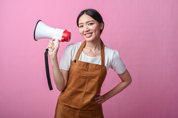 Asian woman in brown apron holding a white and red megaphone, appearing to speak confidently,...