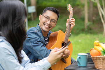 Musical Joy. Young man playing guitar while friend enjoys smartphone outdoors.