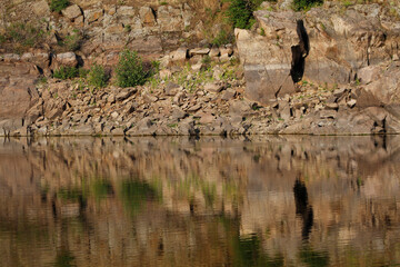 the rocky river bank is reflected in the water
