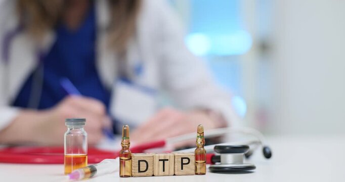 Female doctor takes notes at table near DTP on wooden blocks and medical items on desk. Focus on DTP vaccine and medical practice in modern clinic
