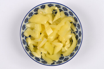 An overhead shot captures a blue and white patterned bowl filled with freshly sliced pale yellow bell peppers, centered on a plain white background
