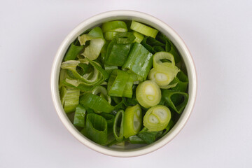 An overhead shot captures a white bowl filled with freshly chopped green spring onions, positioned on the left side of a vibrant green background with ample copy space