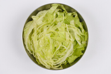 An overhead shot captures a metallic bowl filled with shredded green iceberg lettuce, centered on a plain white background