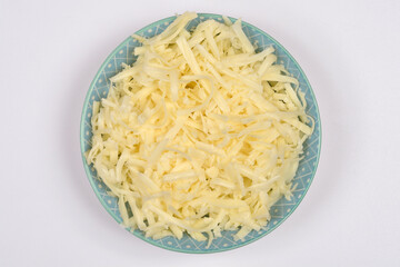 An overhead shot captures a light blue patterned bowl filled with freshly shredded cheese, centered on a plain white background