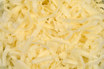 A full-frame, overhead close-up captures a vibrant pile of freshly shredded light yellow cheese, highlighting its intricate texture and various strand lengths