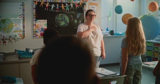 Primary School Children Standing Up, Placing Their Hands on Heart, Performing the Country's National Anthem with Female Teacher Before Geography Lesson. Development of Patriotism in Younger Generation