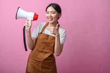 Asian woman in brown apron smiling while holding a megaphone and making an OK hand gesture,...