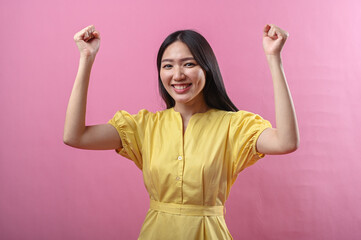 Asian woman in a yellow dress smiling confidently while raising both fists in a celebratory pose....