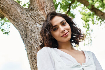 Wavy brown-haired woman enjoying a sunny summer day in a vibrant park setting